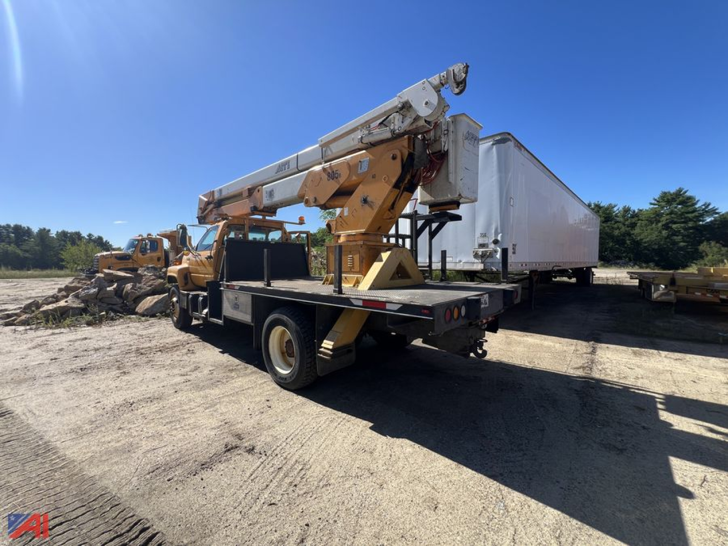 GMC C7500 bucket truck with crane on flatbed trailer, rear view showing boom arm and controls