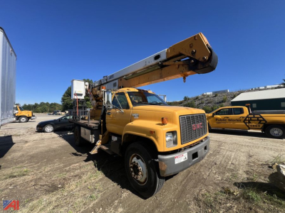 GMC bucket truck with boom raised, yellow utility body, front grille, and stabilizing outriggers visible in a sunny lot.