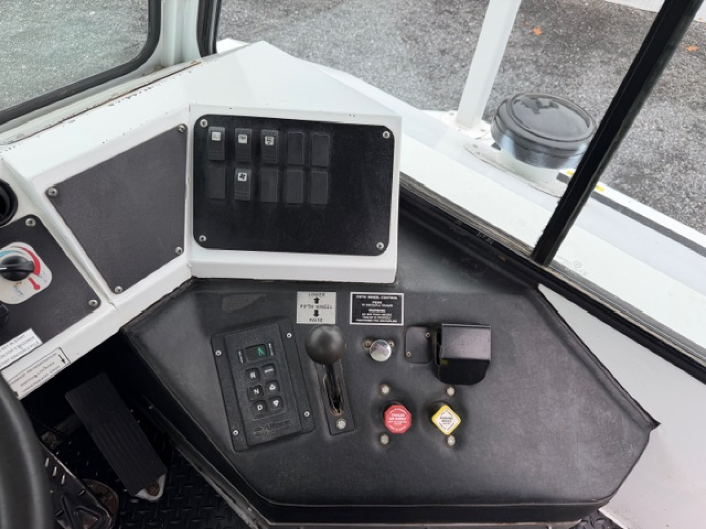 Truck cab dashboard with control panel, switches, and emergency stop; visible labels and gauges on the dash.
