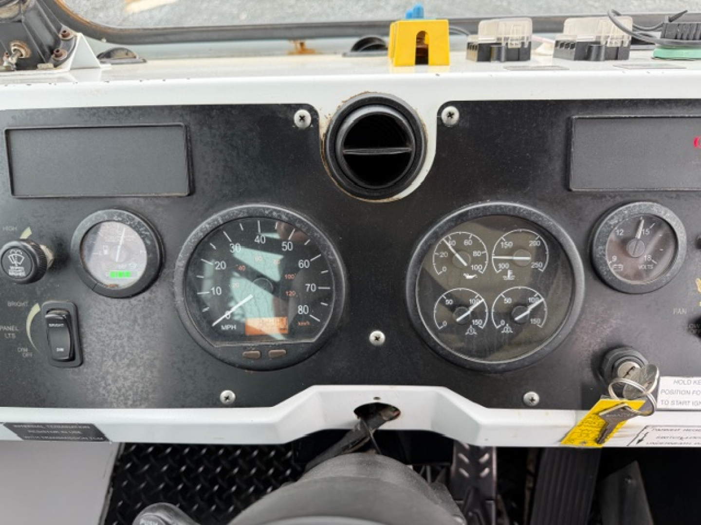 Trucks dashboard panel with multiple round gauges, including speedometer and others, view from passenger side; air vent above dash; key switch and warning markers visible.