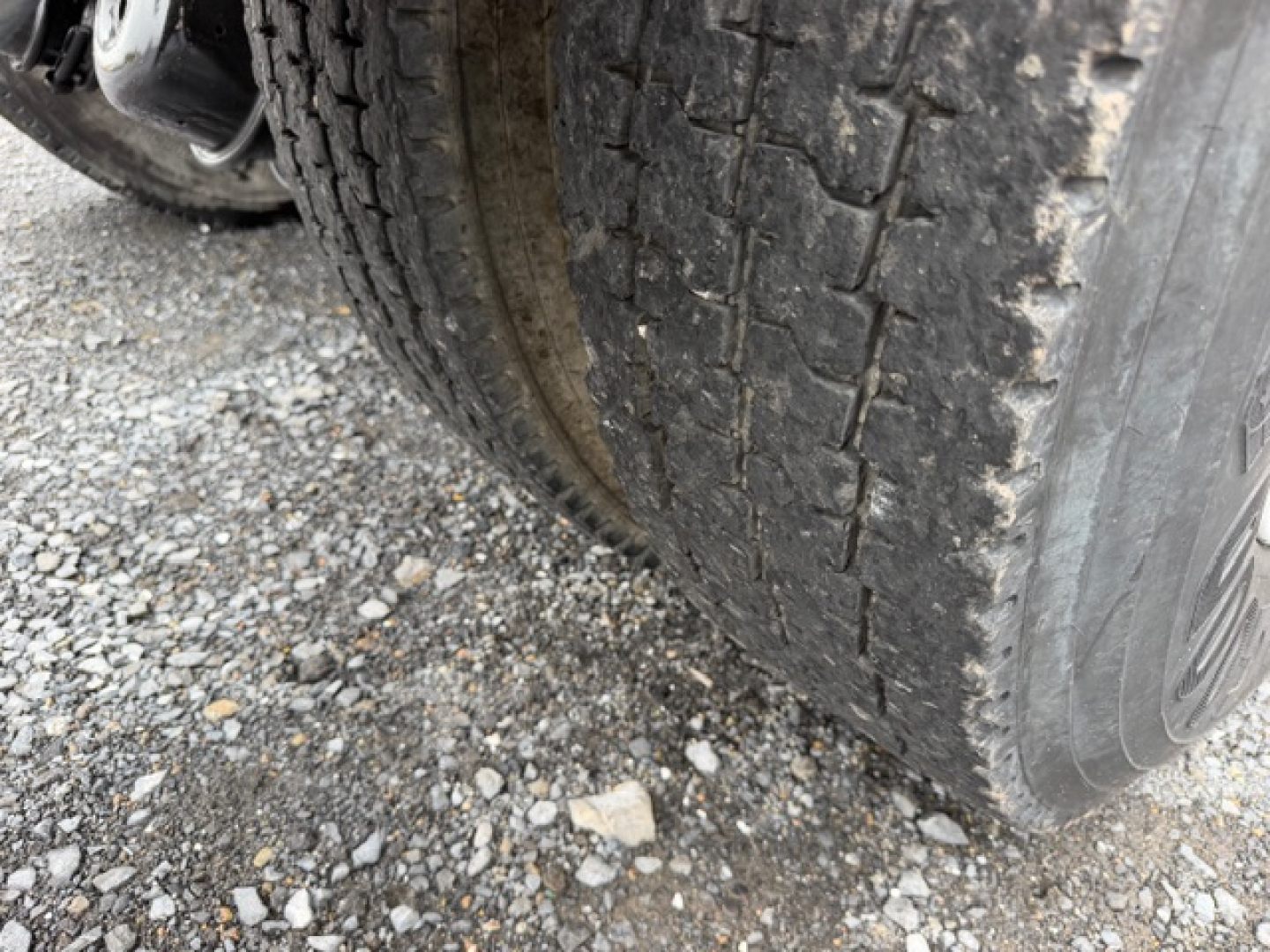Truck wheel and tire tread close-up showing dual rear axle and road grime on gravel surface.