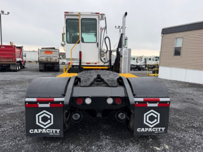 Rear view of a Capacity TJ5000 yard truck with dual rear tires, mudflaps labeled Capacity, and a cab in the distance.