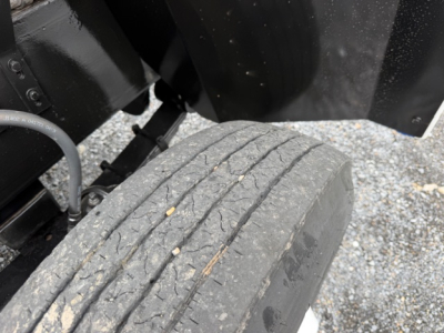 Tire and wheel area of a truck chassis with visible tire tread andComponents nearby; part of the undercarriage and a black painted frame.