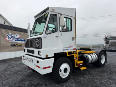 Capacity TJ5000 truck tractor in yard showing front and side, cab with white paint, black grille, and yellow steps; DOT capacity label on door area.