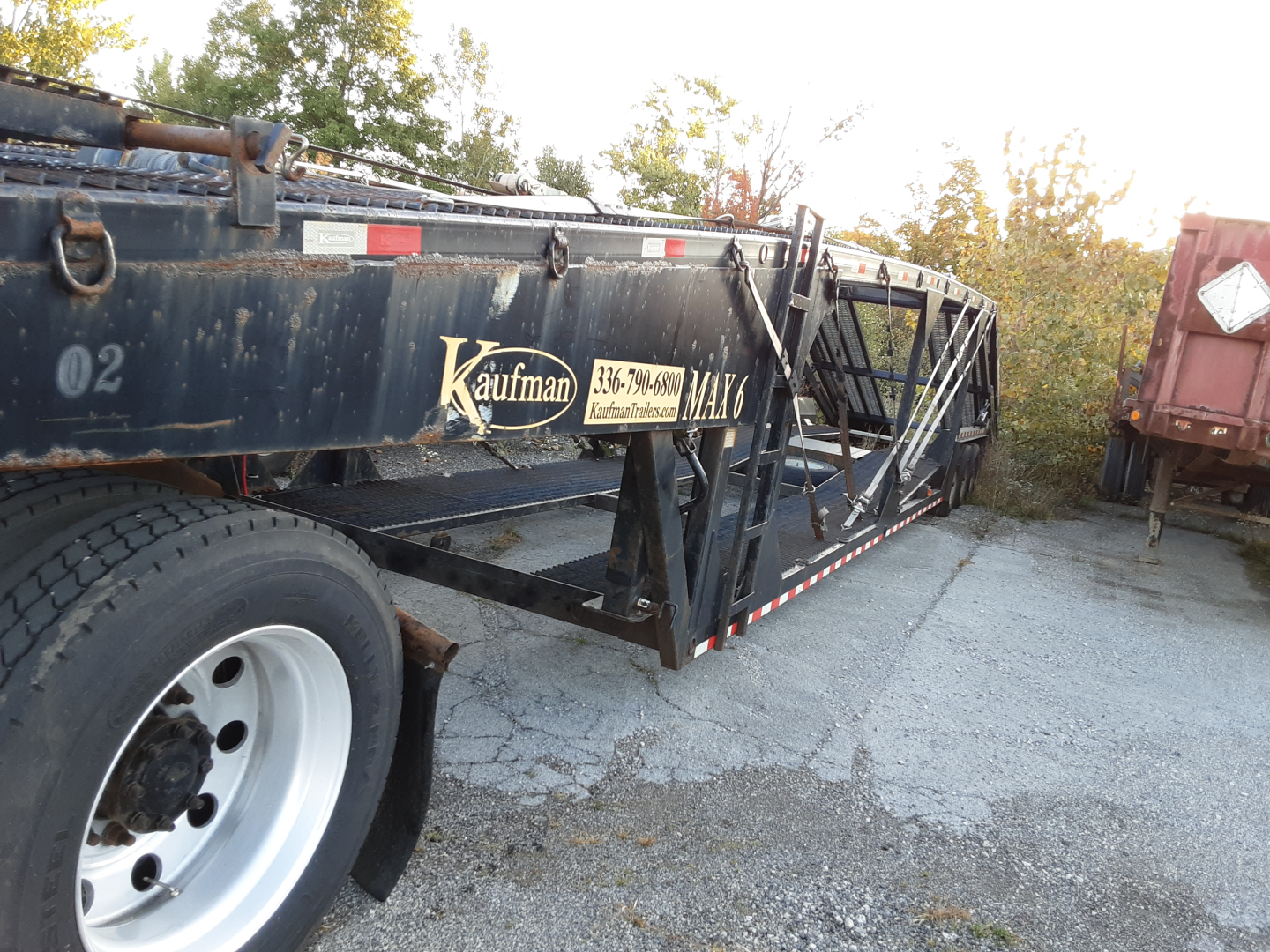Kaufman car carrier trailer in side view showing brand and rails along the frame with a worn finish and big white wheel.