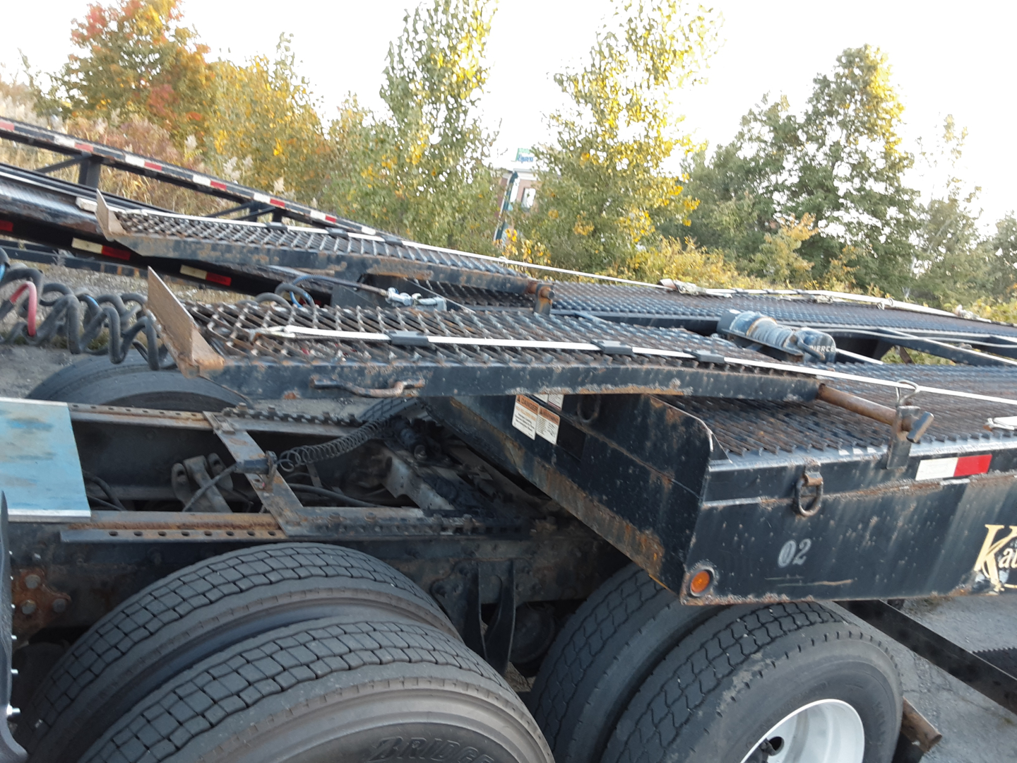 Trailer side showing dual rear axles of a Kaufman car hauler with heavy-duty frame, tires, and metal decking; partial 'Kaufman' branding visible.
