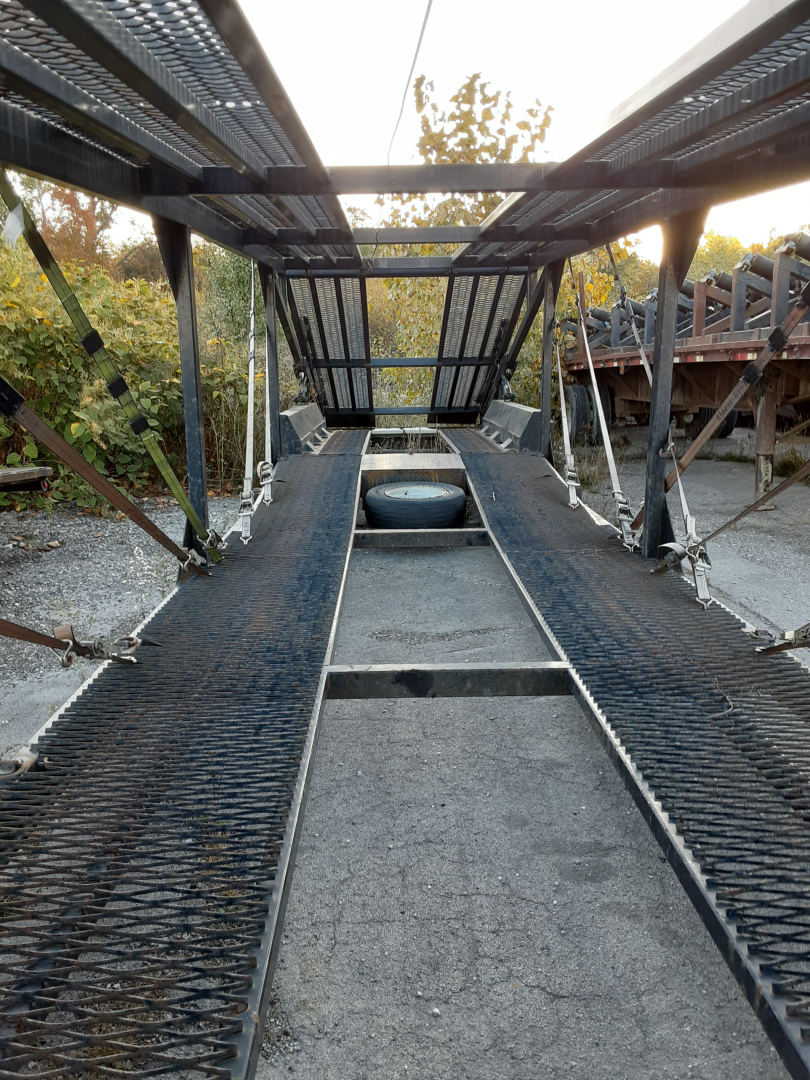 Trailer car carrier frame and deck showing walkway, ramps, and spare tire on bed.