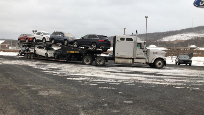 Car carrier trailer with multiple cars loaded on two levels, white cab, long trailer, in a snowy lot.