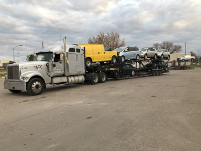 Semi truck cab and multi-car trailer transporting several small vehicles including a yellow van and other cars.