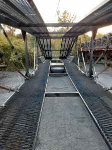 Trailer car carrier frame and deck showing walkway, ramps, and spare tire on bed.