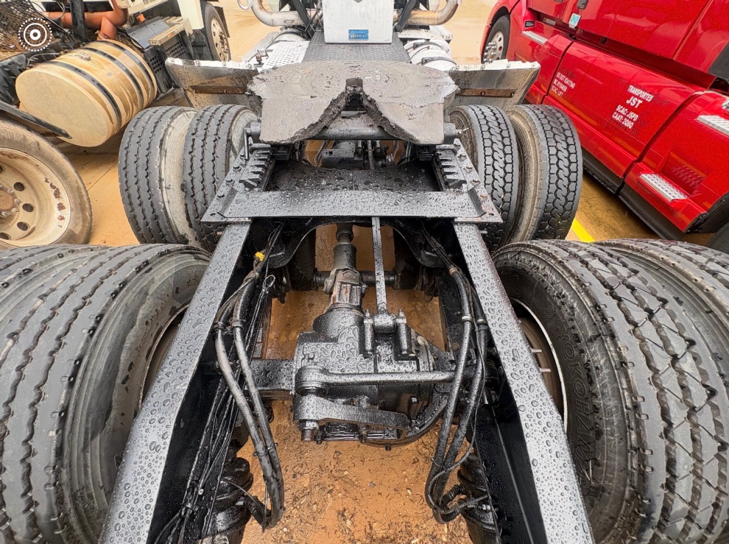 Truck chassis with rear axles and suspension visible, dual rear axles, Dana/S20 differential, rubber tires, and frame rails; wet from rain; components labeled but no legible text.