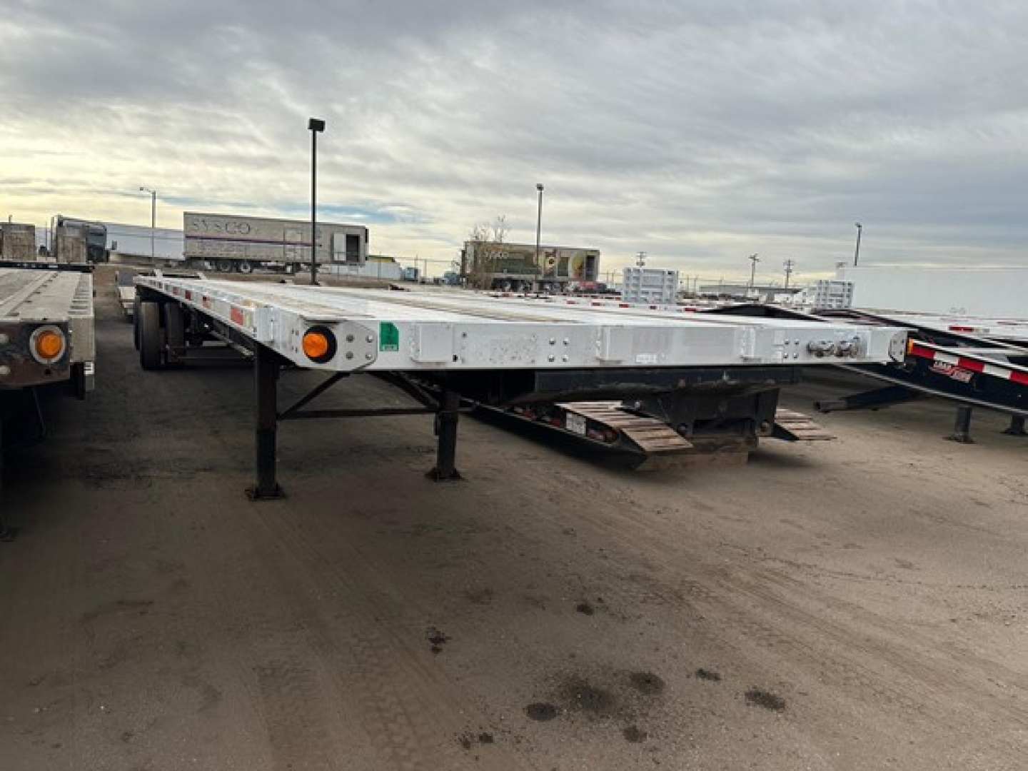 Flatbed trailer showing low deck with tandem axles and orange marker lights at rear.