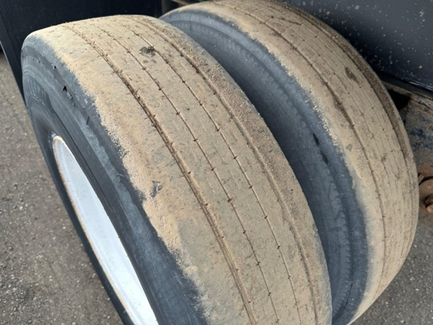 Wide view of a tandem axle on a utility flatbed trailer showing dual tires with dirt on tread and sidewalls.