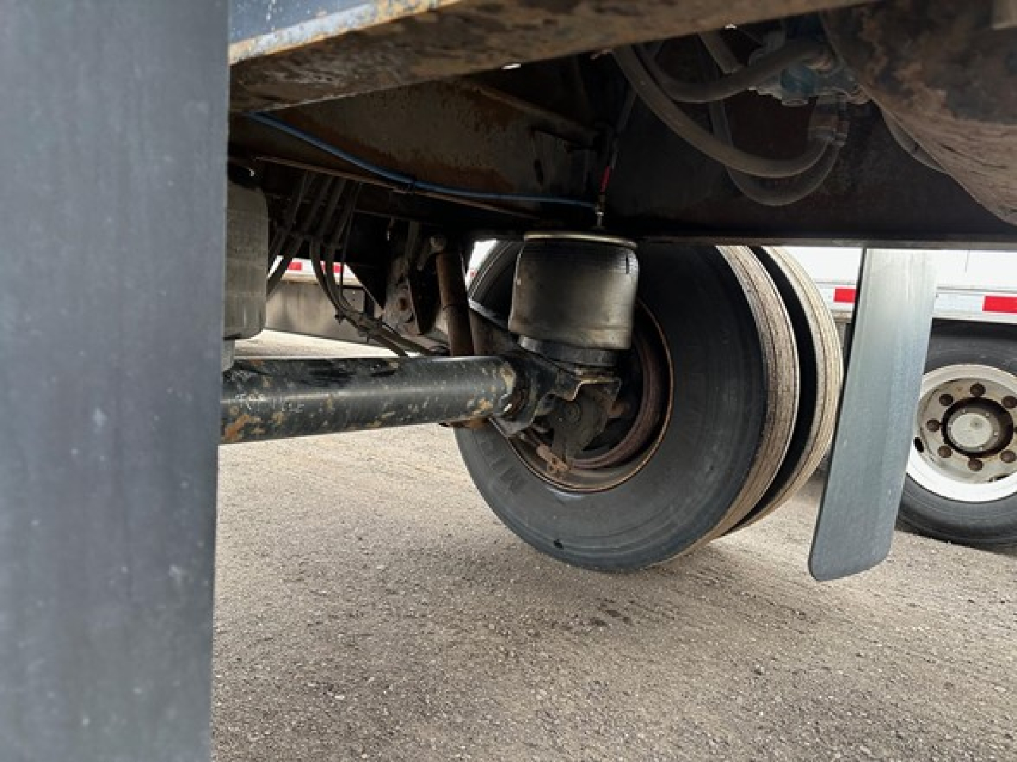 Trailer wheel assembly and undercarriage showing hub, suspension, and tire. Visible components include axle, leaf spring, and underside structure.