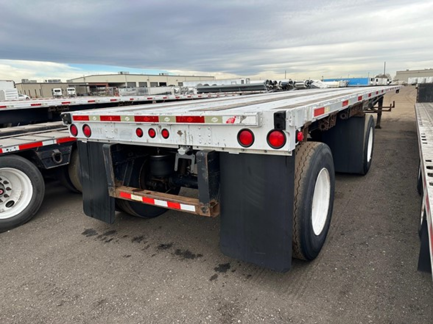 Trailer rear with dual rear axles and mud flaps, Utility flatbed trailer with taillights; shows aluminum frame with red reflectors and black fenders.