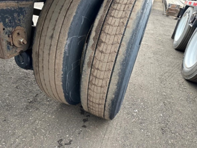 Trailer dual axle tires with worn treads on a flatbed trailer, visible rims and part of the frame; no other text visible.