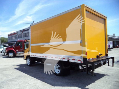 Isuzu NPR HD box truck with yellow cargo area and rear ramp, side view showing cargo box and dual rear wheels