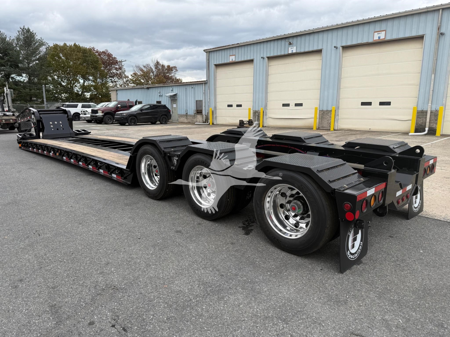 Lowboy trailer showing dual rear axles and long flatbed with wheel fenders and ramps, Fontaine 55Lcc series trailer in a lot.