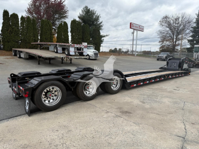 Lowboy trailer from side showing long flat deck with multiple axles and wheels, Fontaine 55Lcc W model designation not visible, open yard with other trailers in background.