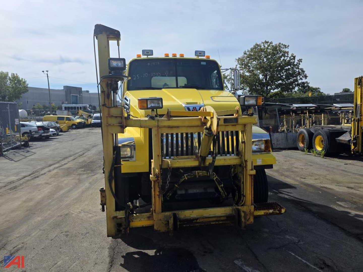 A yellow Western Star 4700 SF truck with wing and front equipment for stone spreading, showing front view.