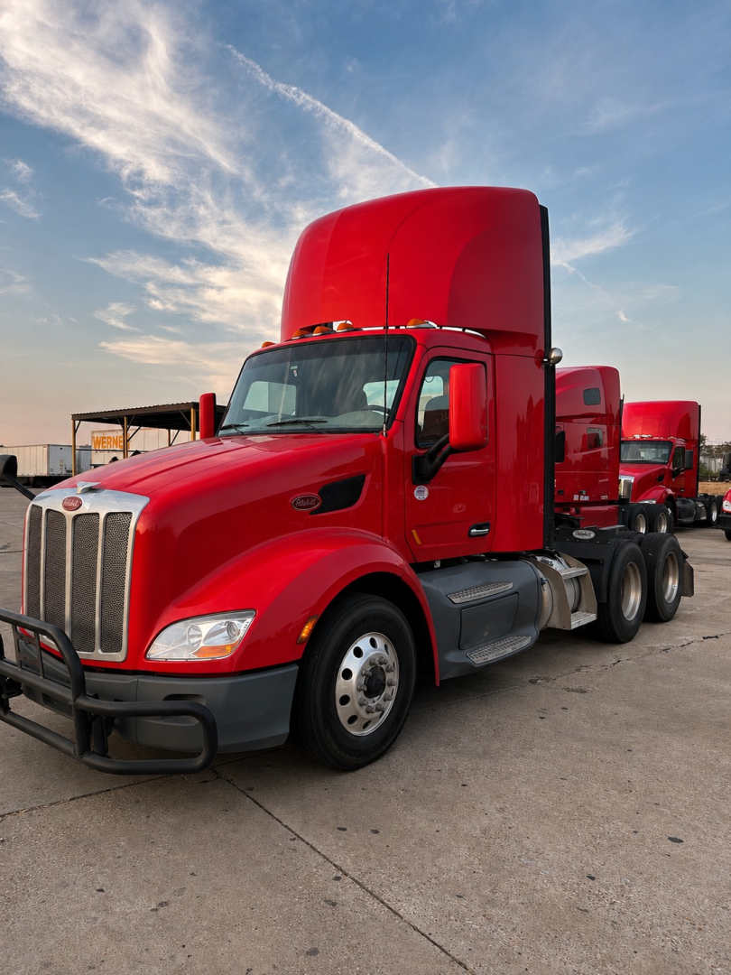 Peterbilt 579 conventional daycab truck in red with sleeper cab raised, front grille and dual rear axles visible.