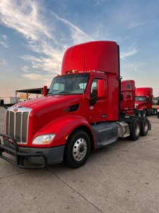 Peterbilt 579 conventional daycab truck in red with sleeper cab raised, front grille and dual rear axles visible.