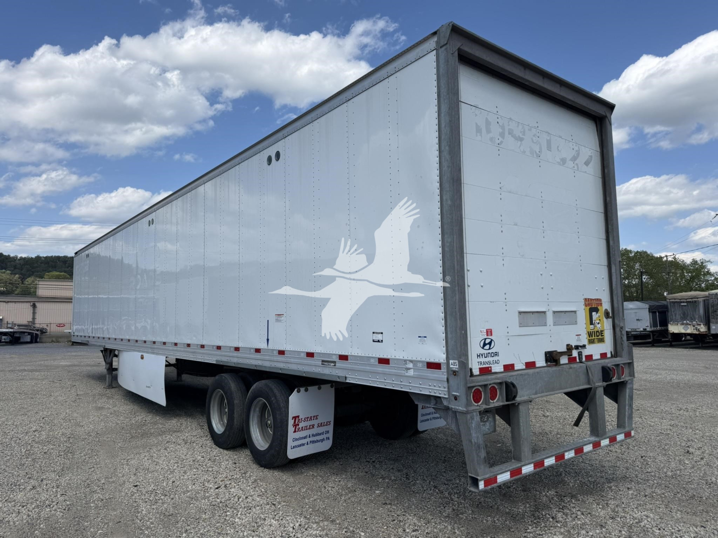 Hyundai roll door trailer van with triple-axle rear, white box, faded logo on side, rear doors closed, gravel lot background