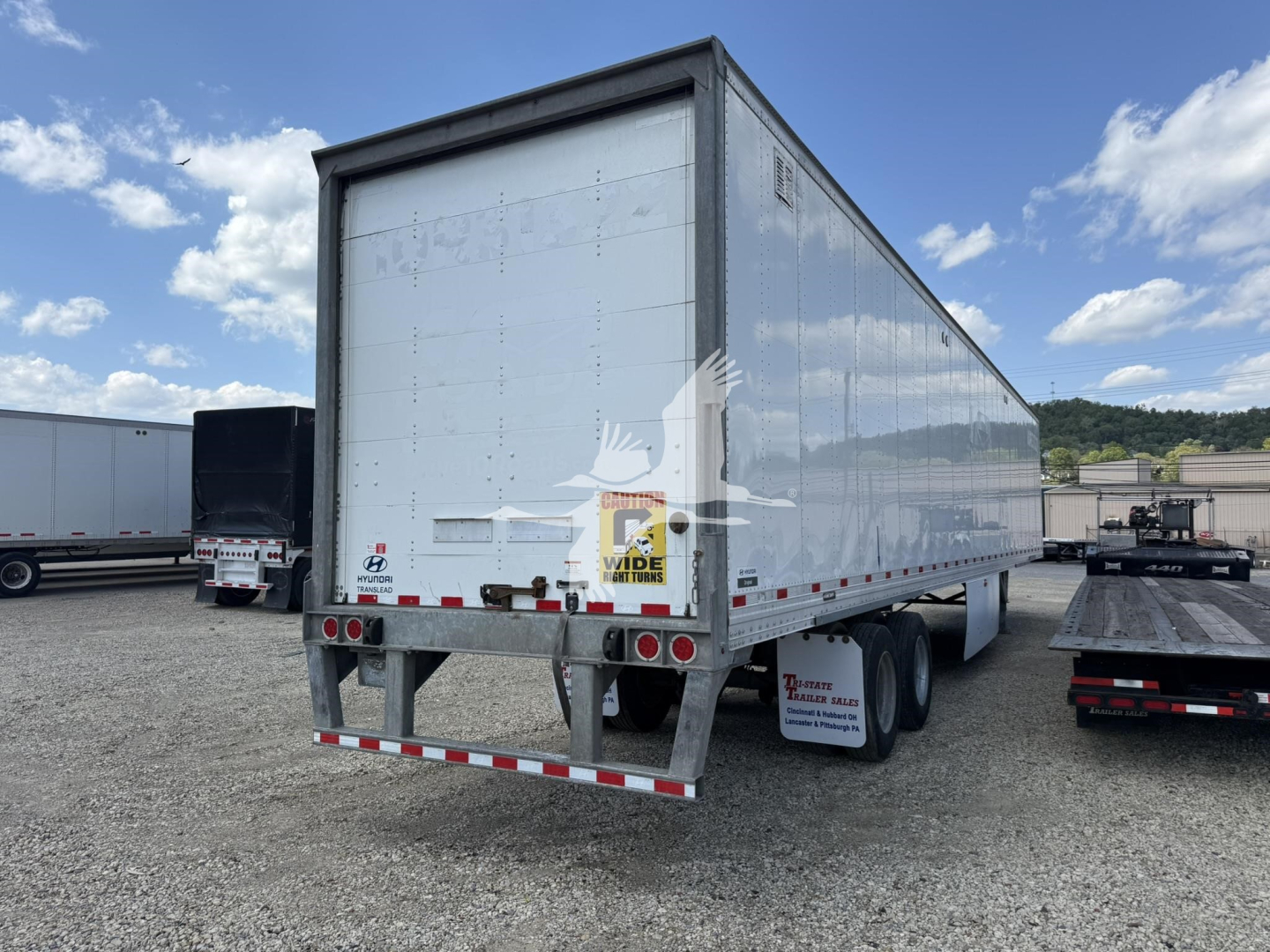 Hyundai roll door trailer van with rear doors, dual rear axles, white exterior, light scuffs and a Wide Load sticker on the back.
