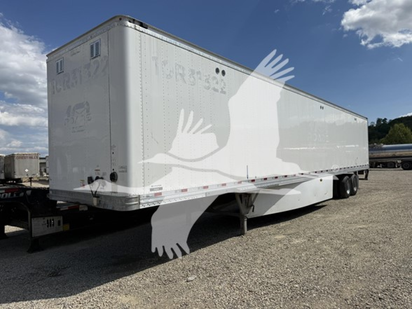 Trailer side and rear view of a white Hyundai roll door van trailer in a gravel lot.