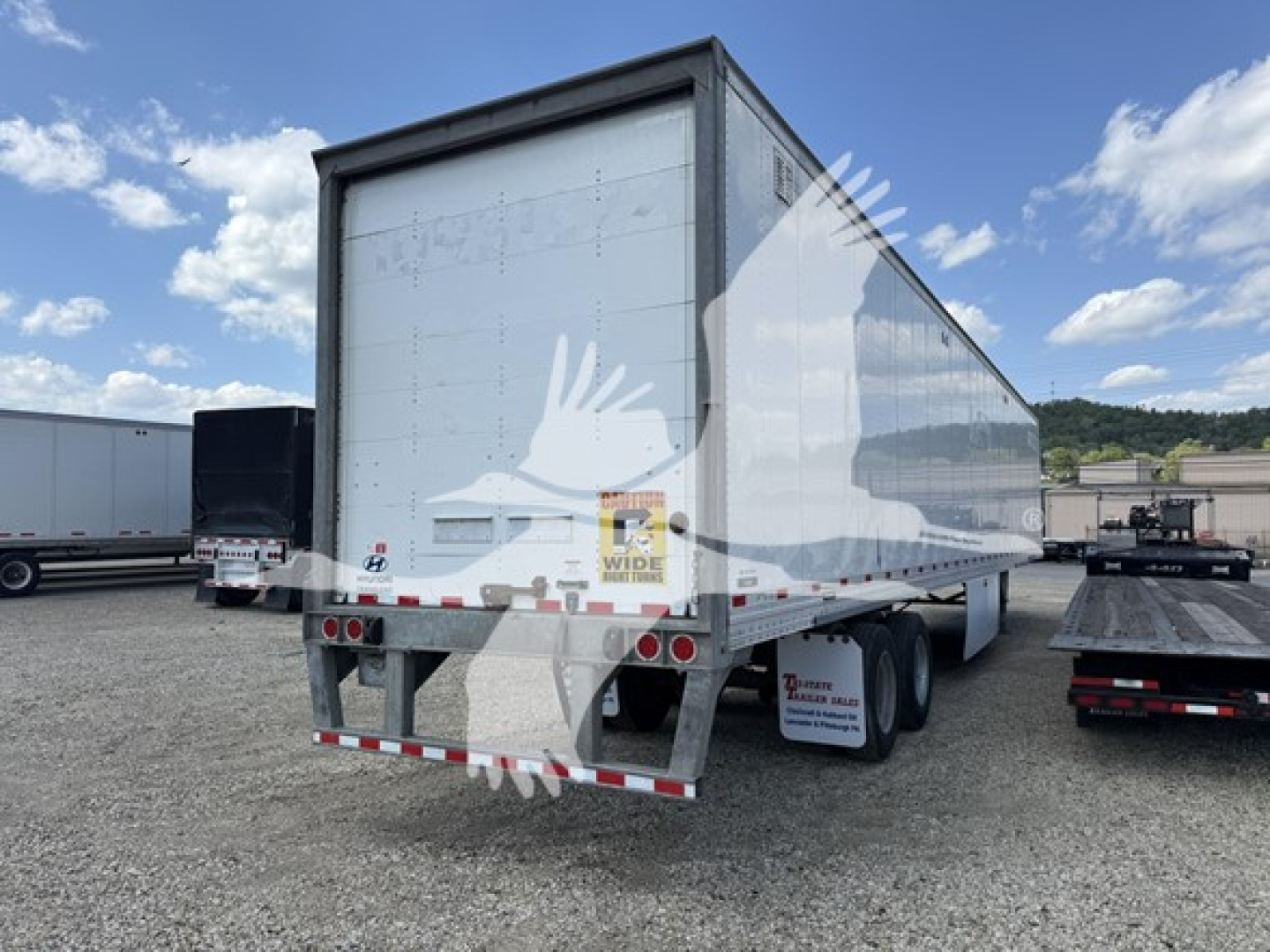  trailer van rear view showing roll-up door and cargo area, Hyundai logo on side, trailer tires and reflective tape