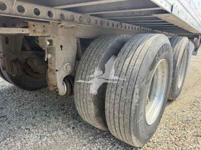 Triple-axle trailer undercarriage showing dual rear tires and leaf spring suspension with rust-free frame. Visible: wheels, tires, axle housing, and frames.