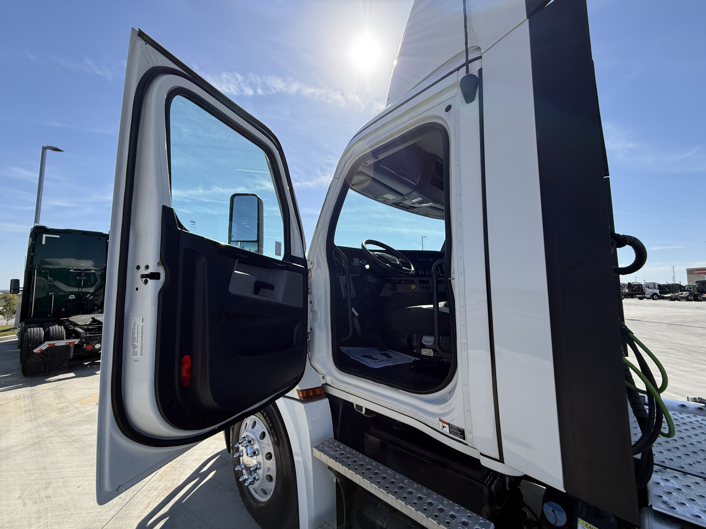 Truck cab interior and open door of a Freightliner day cab showing door panels and entry step with chrome wheels visible.