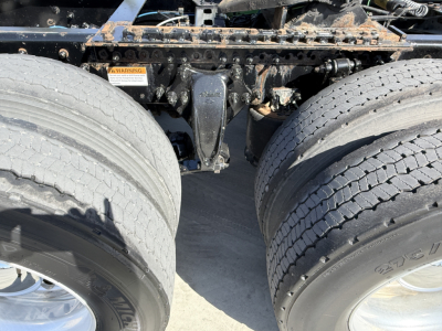 Freightliner truck rear dual tires and suspension components in view showing frame rails and fifth wheel area with some rust and dirt.