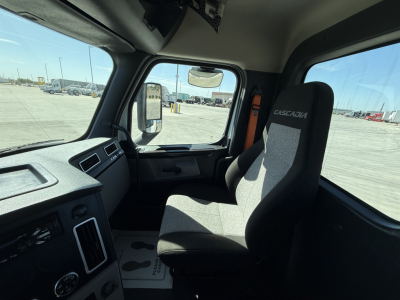 Truck cabin interior of a Freightliner PT126064S T daycab showing driver seat and dashboard area, steering wheel, side window, and center console.