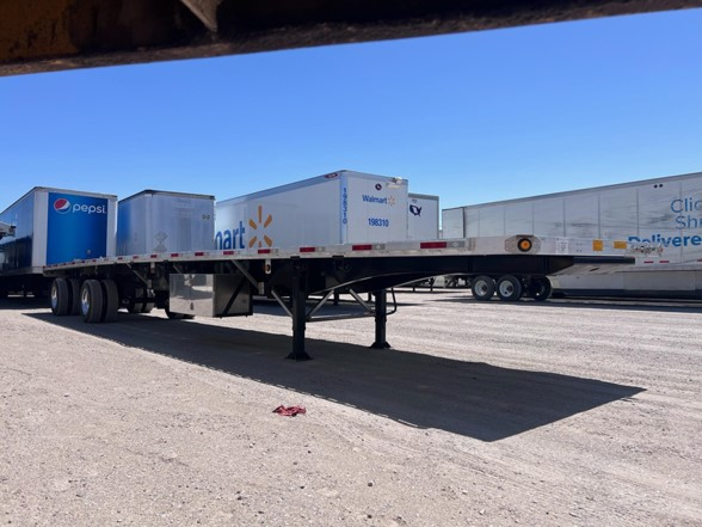 Trailer flatbed with parked dry vans on a lot, Utility combo flatbed trailer in view.