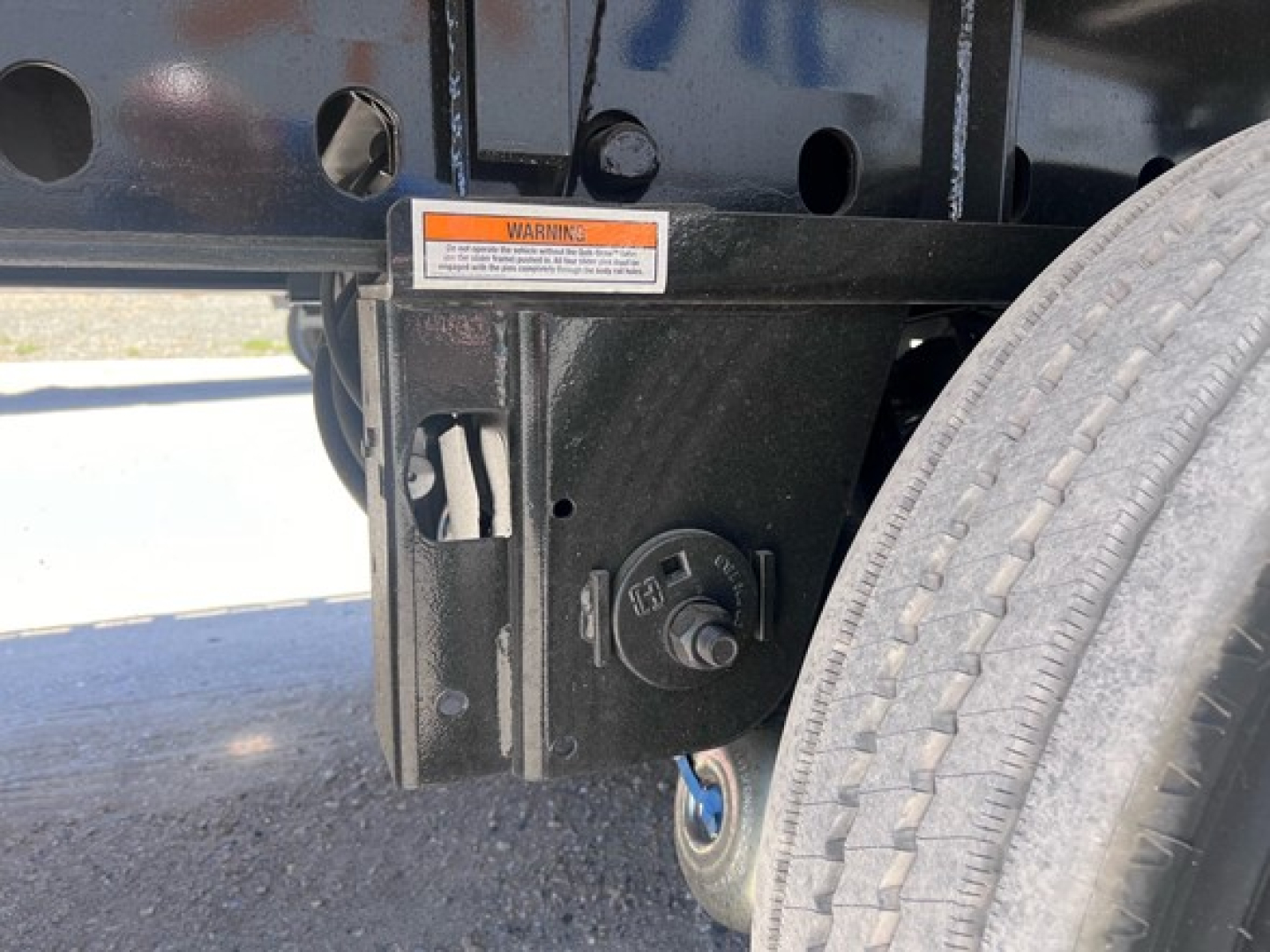 Trailer hitch/frame showing coupling mount with warning label, and a large tire on the right side of a flatbed trailer.