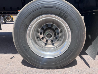 Trailer wheel and tire showing steel aftermarket rim with lug nuts and center cap.