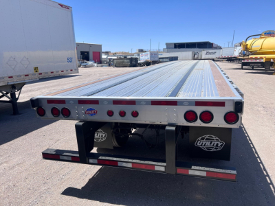 Flatbed trailer rear view showing Utility brand plate and taillights, with reflective tape along edge and mud flaps labeled Utility.