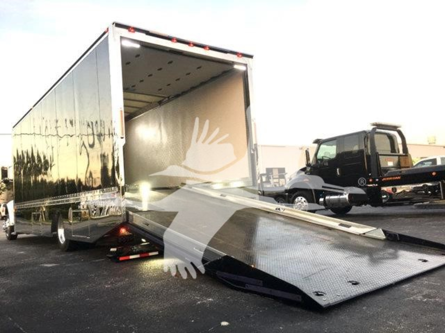 Peterbilt 337 rollback truck with open cargo box and folded rear ramp, black cab in background.