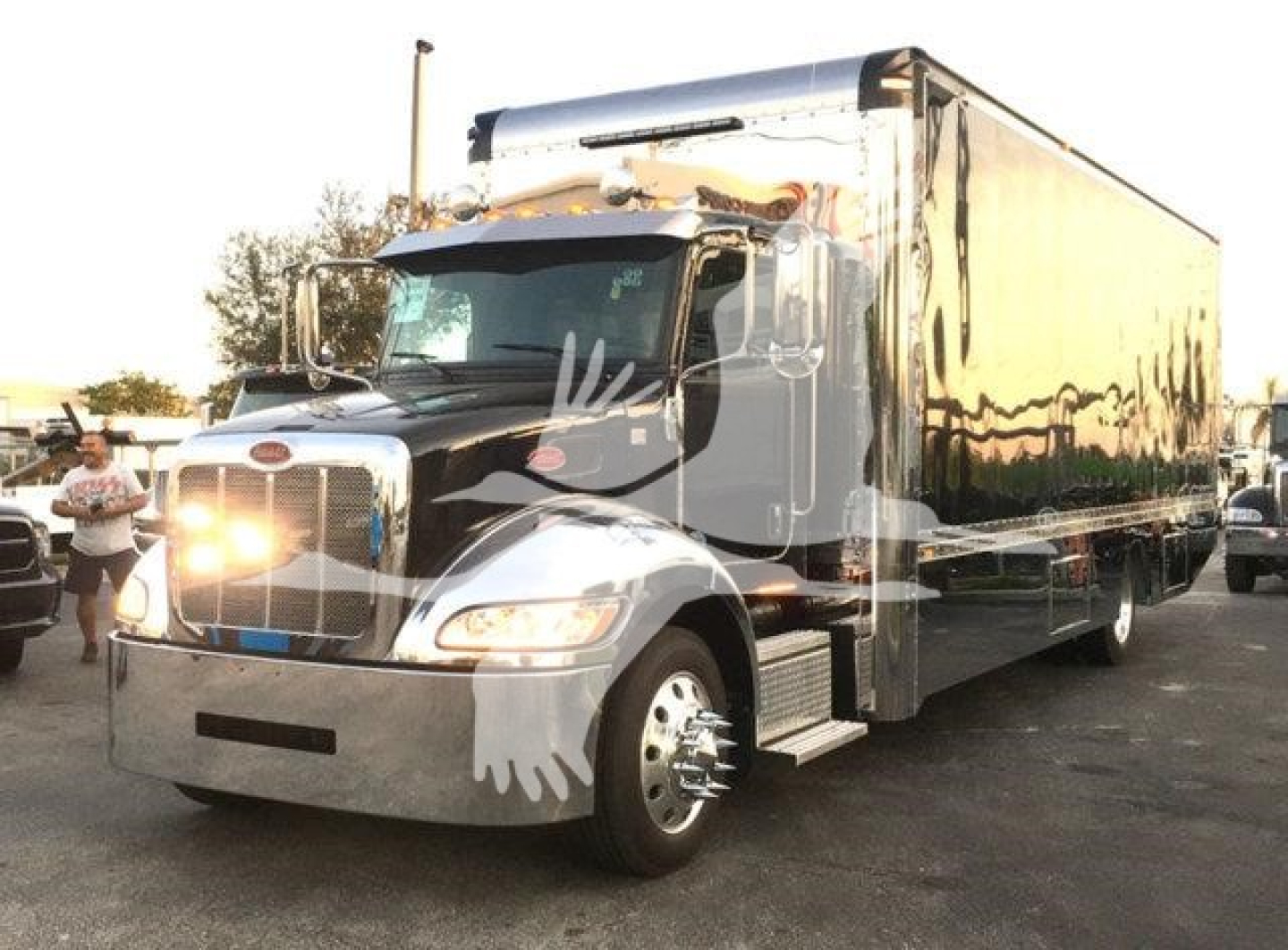 Peterbilt 337 rollback truck in showroom lot with chrome bumper and large box trailer, front headlights on, stock number J56602 information visible in the listing context.
