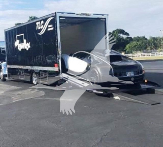 Truck with rollback trailer showing TLC logo on black cargo box and Peterbilt day cab, front grille visible, loading ramp on ground.