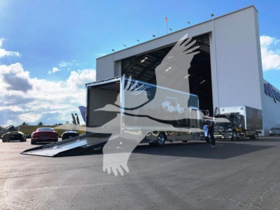 Truck terminal with a white Peterbilt 337 rollback truck being loaded into a large service bay; ramp extended; clear blue sky
