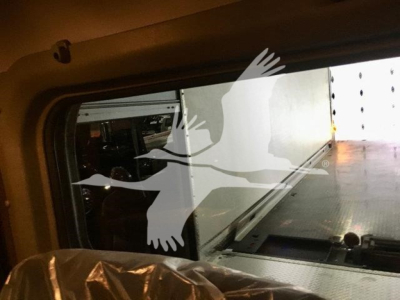 Truck cab interior window view showing loading area and side of rollback truck bed; parts of trailer bed visible through window
