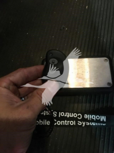 Key fob and blank metal plate in hand on a dark surface.