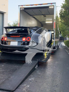 Peterbilt 337 sports car on a rollback truck bed, loaded in a rear-view towed position inside a transport trailer.