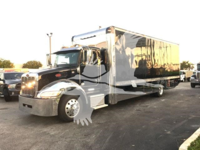 Peterbilt 337 rollback truck with a large chrome bumper and a long black and silver box body, front grille with round headlights.