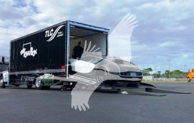 Peterbilt 337 truck on a rollback trailer with ramps deployed, loading a car into a black TLC branded trailer.