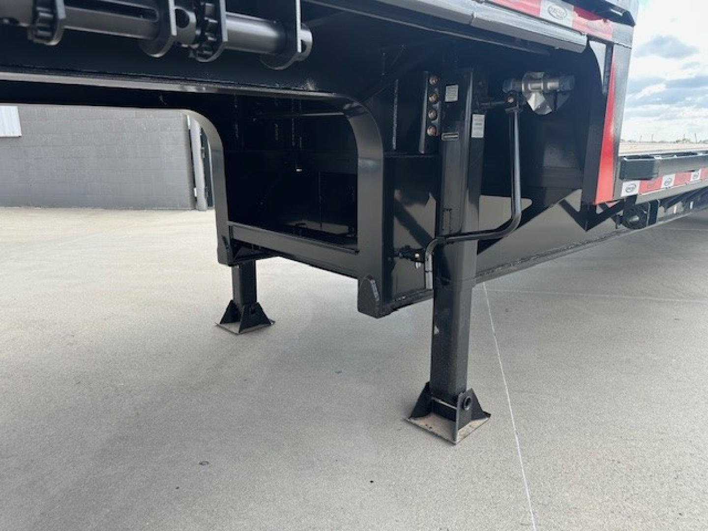 Trailer hitch area showing landing gear and undercarriage of a 2027 Dura Haul drop deck trailer with spread tail ramps, black steel frame, and stabilizer legs.