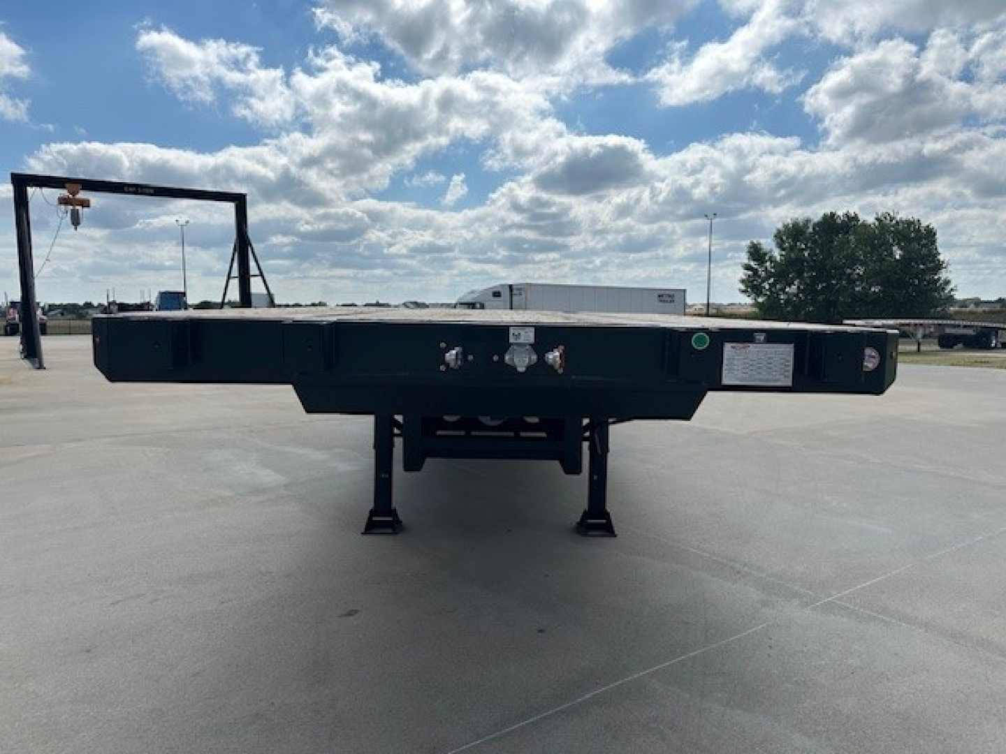 Trailer rear view showing drop deck trailer with spread axle, low landing gear and ramps folded under deck