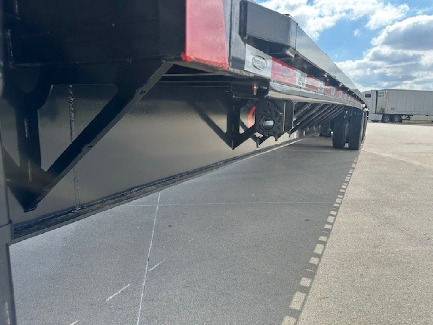 Trailer side view showing drop deck trailer with undercarriage and ramps, low angle perspective.